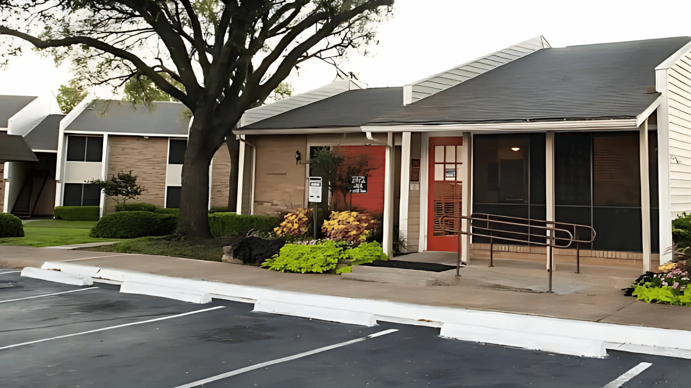 a parking lot with a row of apartments and a tree at The Meadows on Merrill