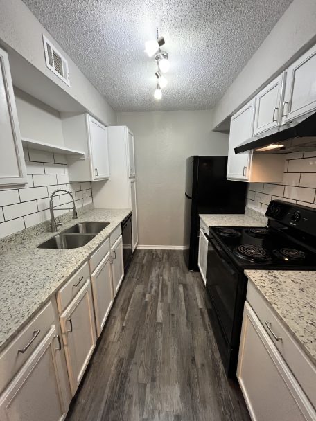 a kitchen with white cabinets and black appliances at The  Discovery Park Life Apartments