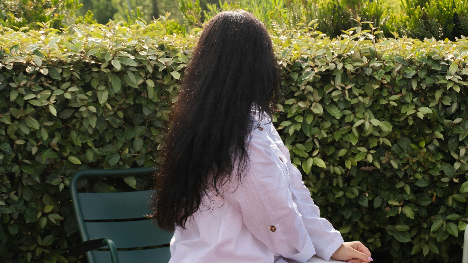 A person with long dark hair sitting outdoors.