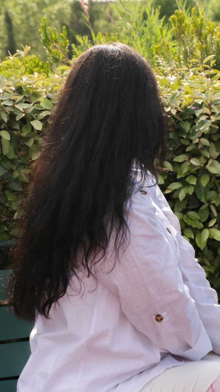 A person with long dark hair sitting outdoors.