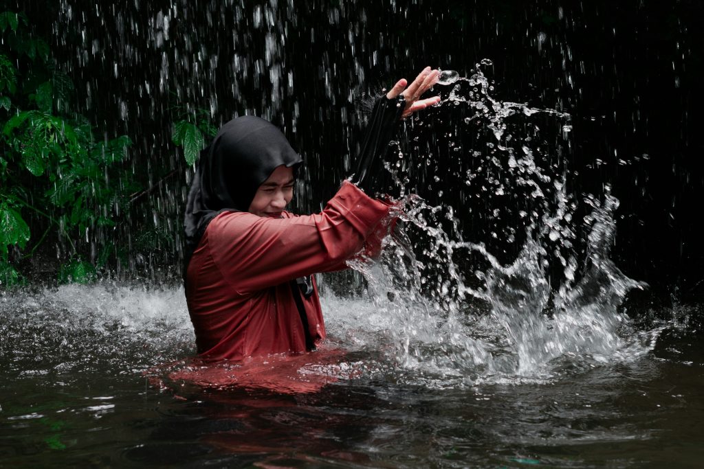 A person in a hijab and red shirt splashing water in a waterfall