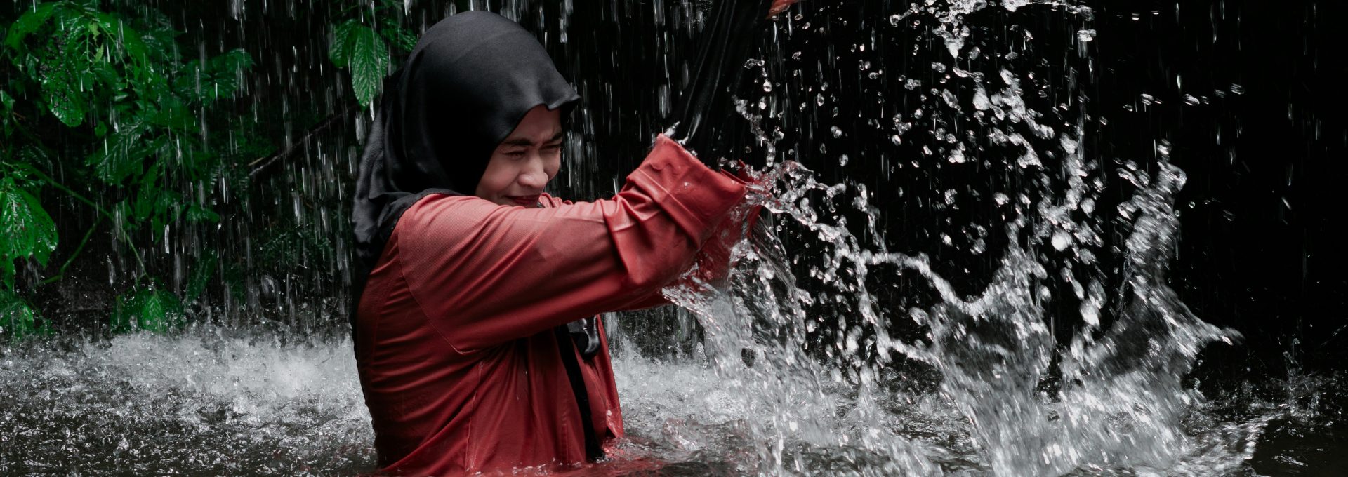 A person in a hijab and red shirt splashing water in a waterfall