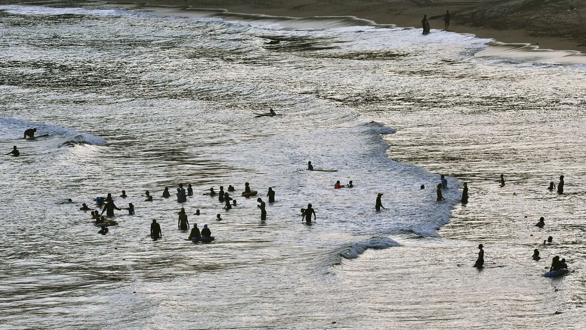 Silhouettes of people swimming and surfing in the ocean waves at a beach
