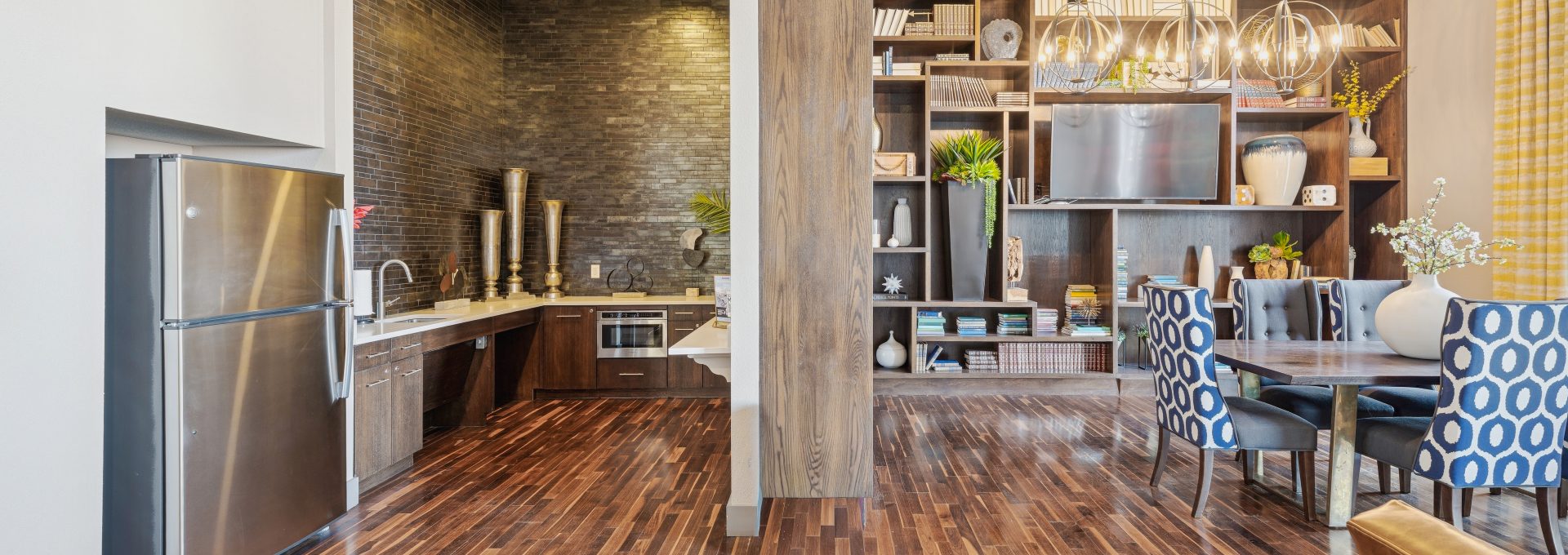A full size kitchen, tv, bookshelves, and a table with blue chairs