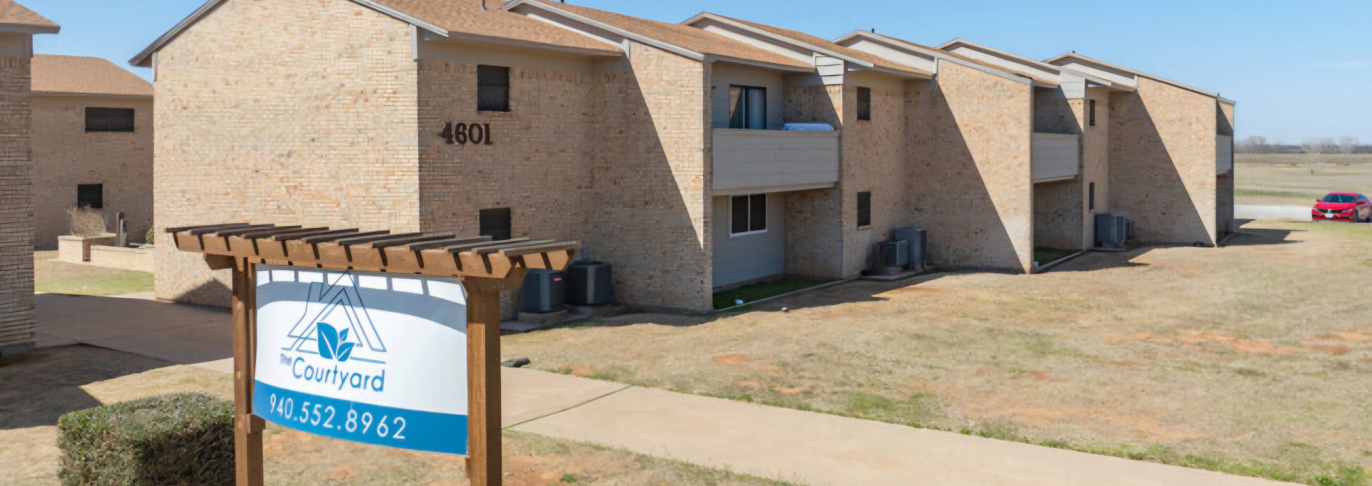 the sign for the apartment complex in front of a grassy area at The  Courtyard