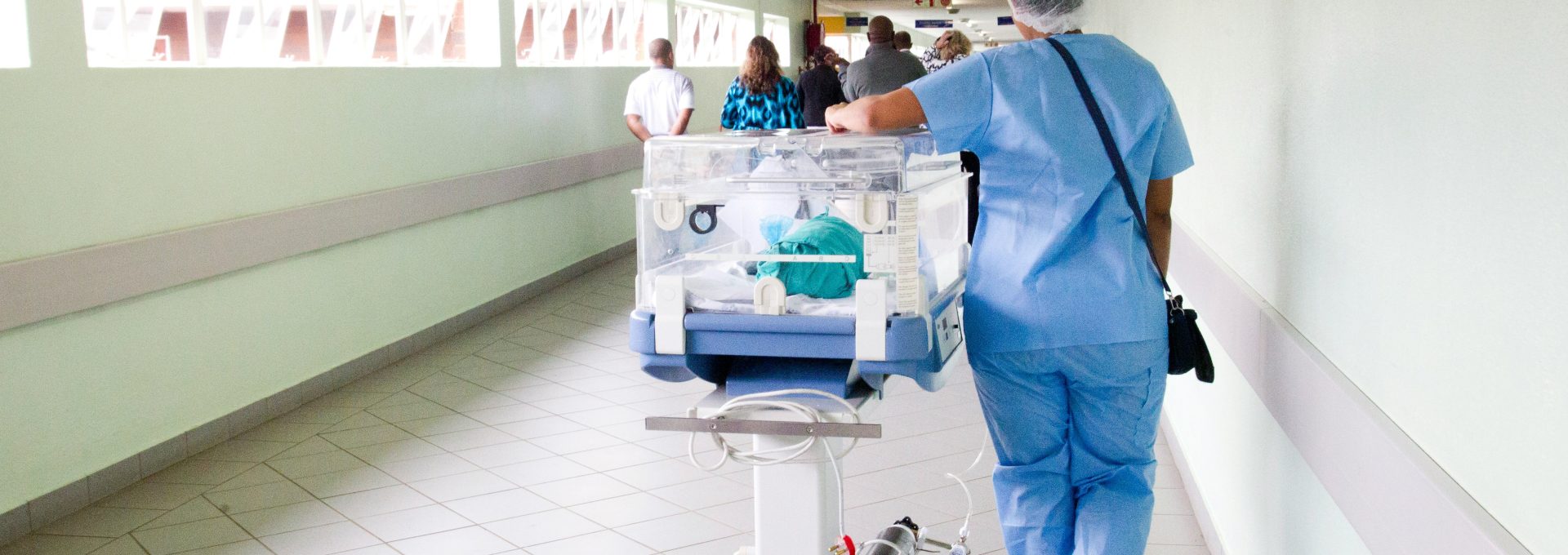 person walking on hallway in blue scrub suit near incubator