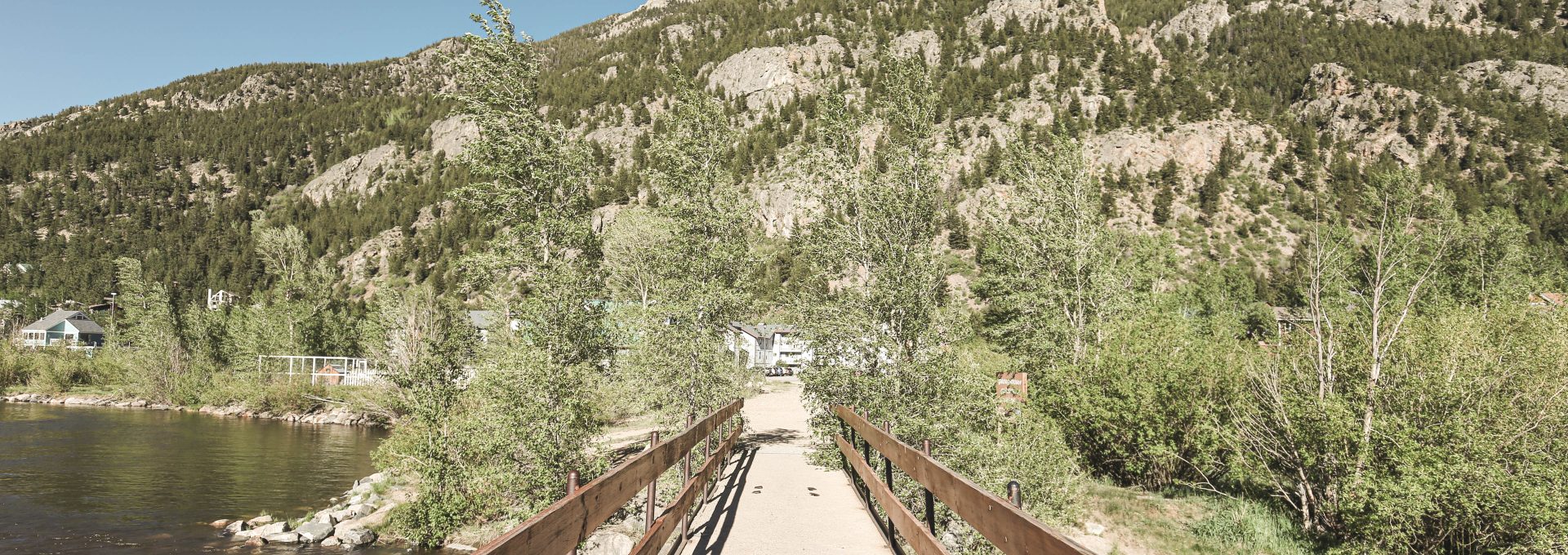 a wooden bridge over a river with mountains in the background at The Bighorn Crossing