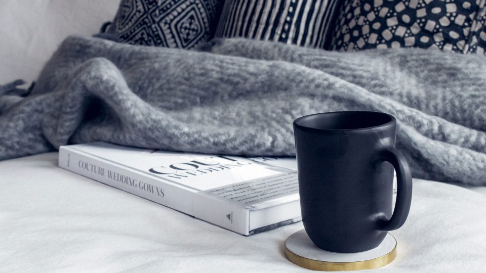 a black coffee cup sits on a bed with a blanket at The Legacy at Veramendi