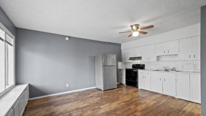 an empty kitchen with a white refrigerator and hardwood floors at The Arden Arms Apartments