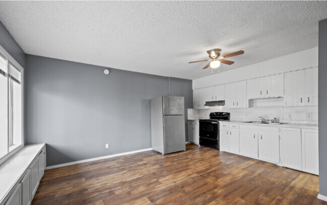 an empty kitchen with a white refrigerator and hardwood floors at The Arden Arms Apartments