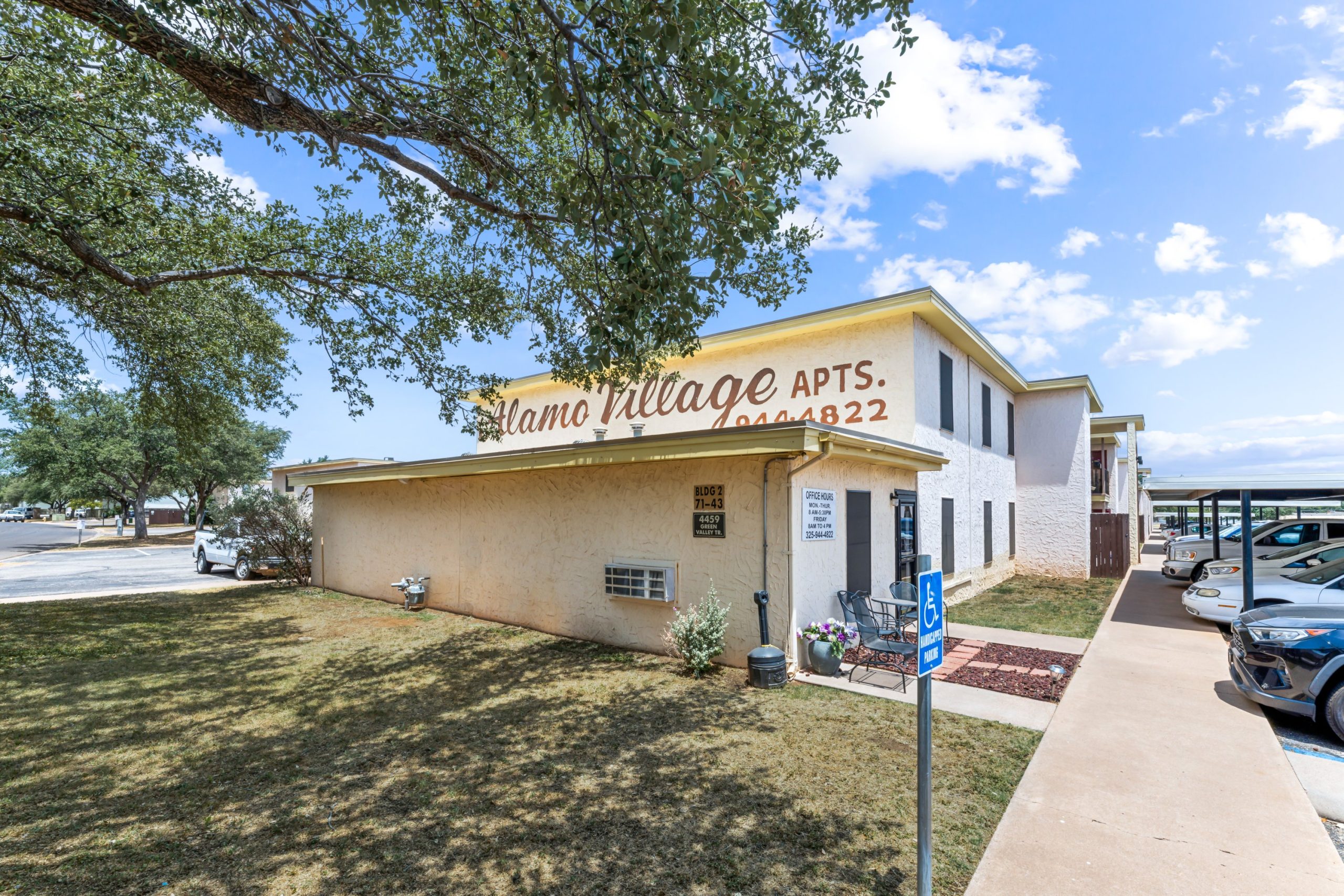 the outside of a motel with a parking lot and trees at The Alamo Village Apartments