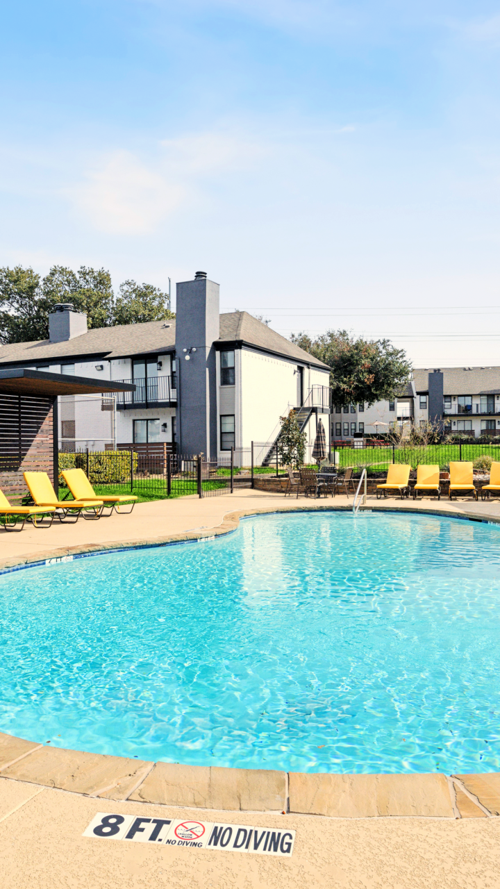 Swimming pool with yellow lounge chairs and shaded cabanas at Brookbend Apartments in Carrollton, Texas