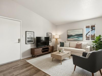 Furnished living room with sofa, accent chair, media console with TV, and private balcony access at Country Gables in Glendale, AZ