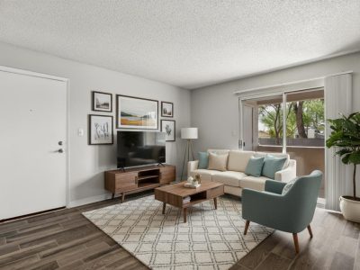 Furnished living room with sofa, accent chair, and TV console with patio access at Country Gables in Glendale, AZ