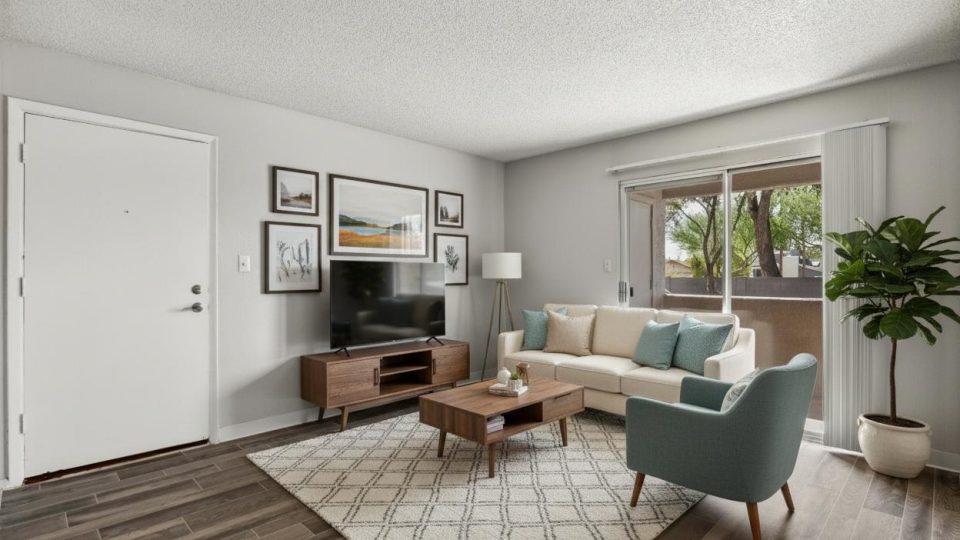 Furnished living room with sofa, accent chair, and TV console with patio access at Country Gables in Glendale, AZ