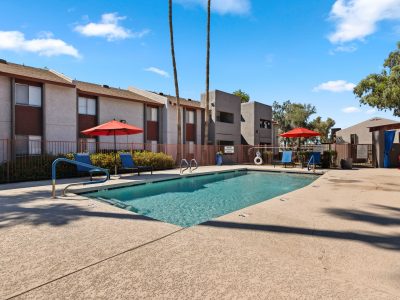 Resort-style swimming pool with red umbrellas, lounge seating, and palm trees at Country Gables in Glendale, AZ