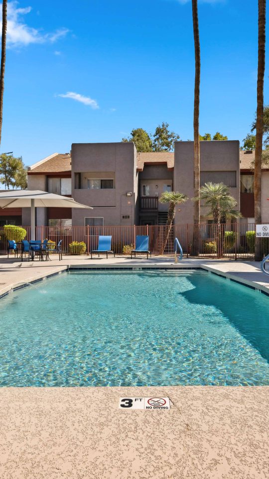 Community swimming pool surrounded by lounge seating and shade umbrellas at Country Gables in Glendale, AZ