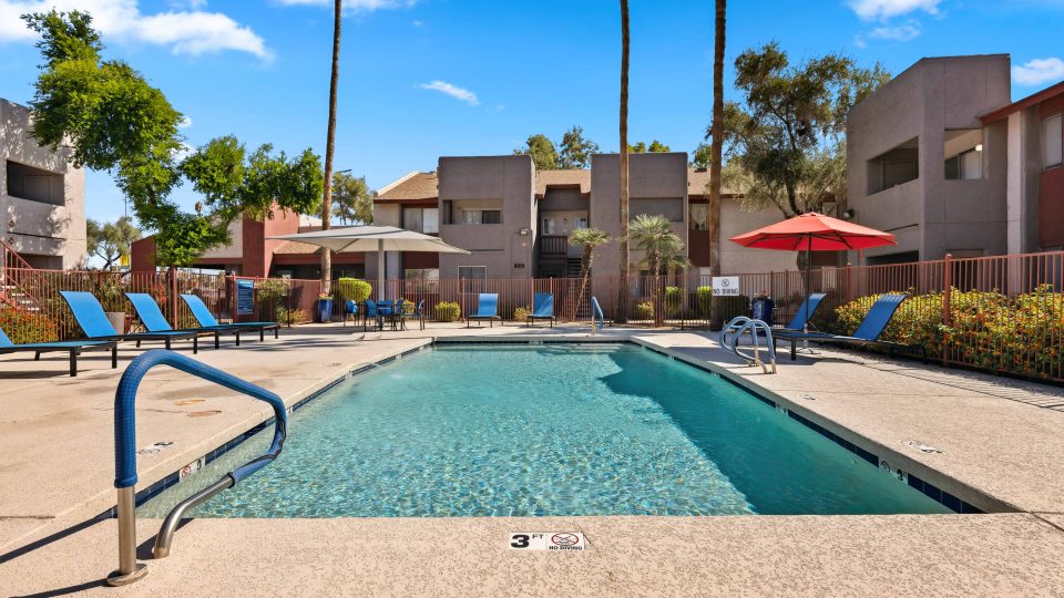 Community swimming pool surrounded by lounge seating and shade umbrellas at Country Gables in Glendale, AZ