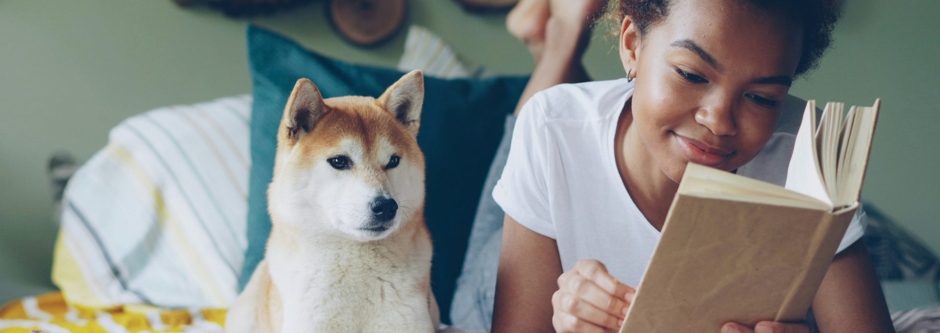 Woman reads a book on bed with her dog.