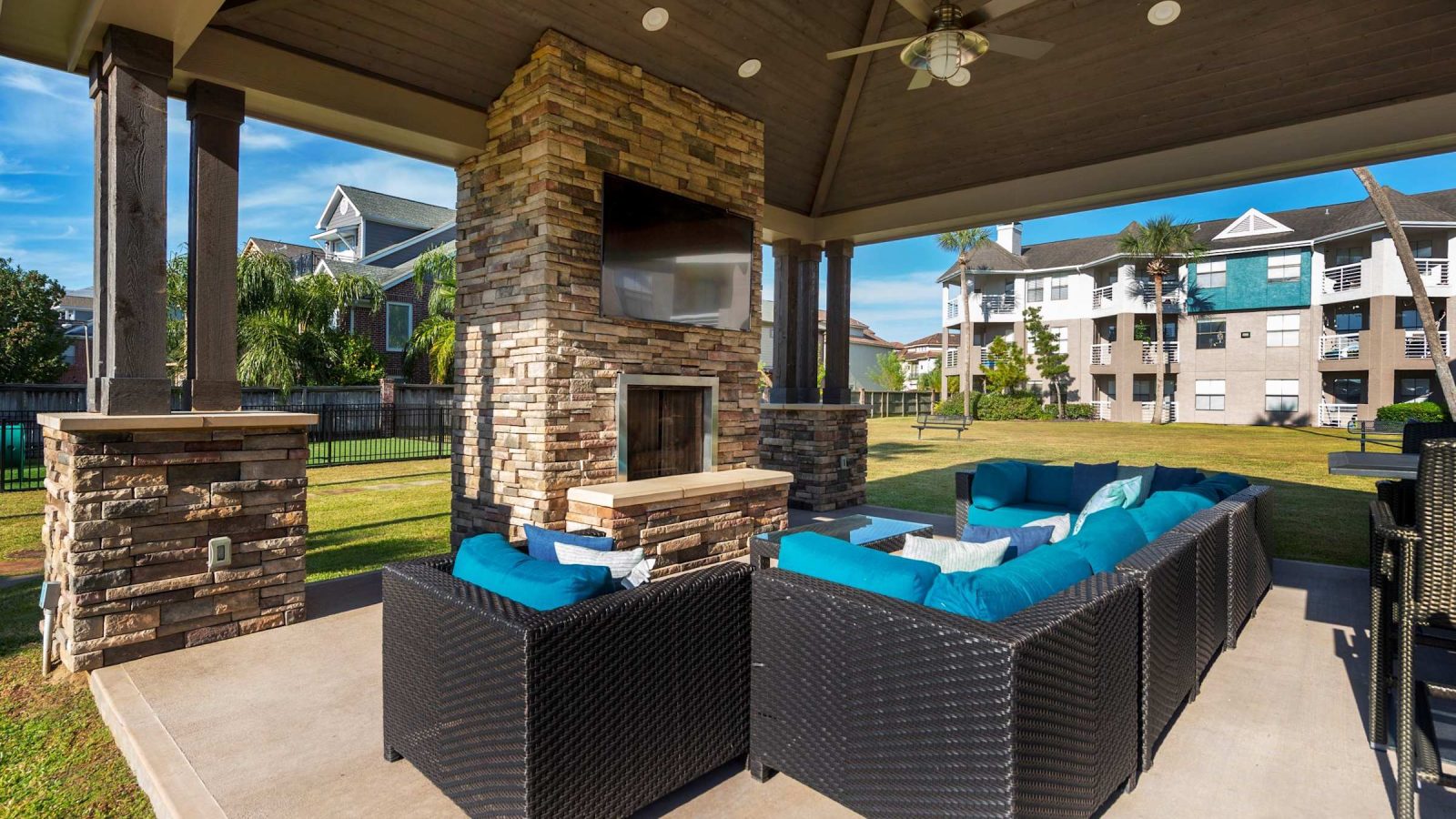Covered outdoor lounge with stone fireplace, TV and cushioned seating at Anchor at South Shore in League City, TX
