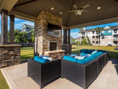 Covered outdoor lounge with stone fireplace, TV and cushioned seating at Anchor at South Shore in League City, TX