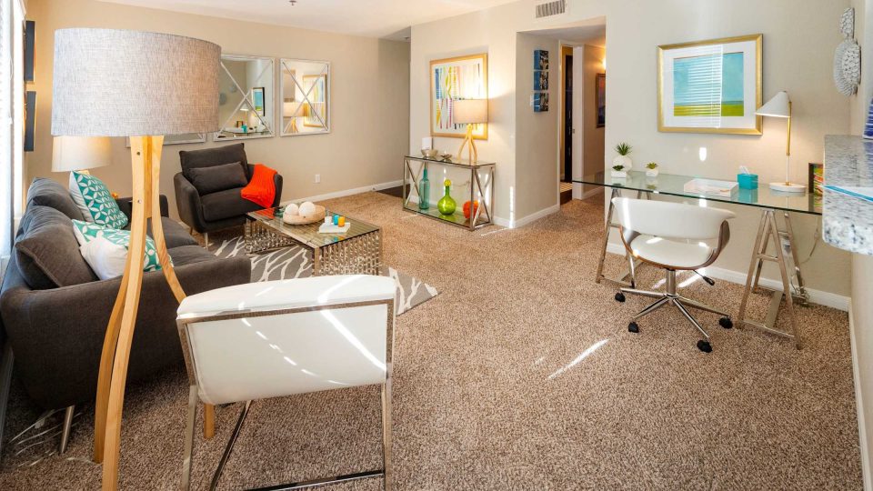Spacious staged apartment living room with seating area and workspace at Anchor at South Shore in League City, TX