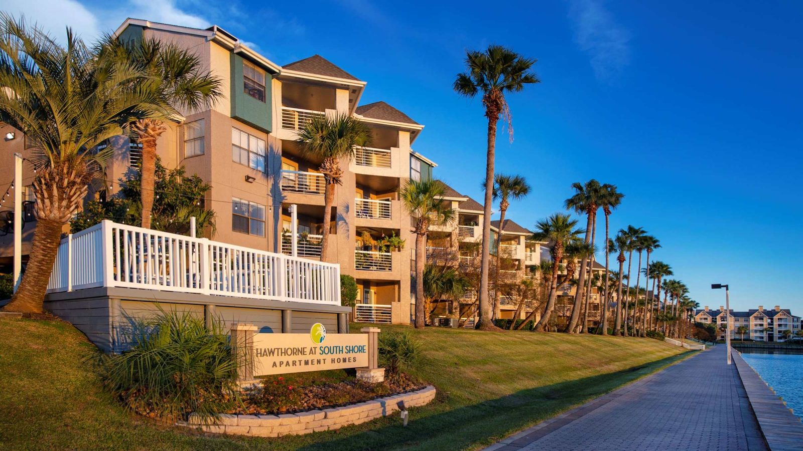 Waterfront apartment building exterior with monument sign, boardwalk and marina at Anchor at South Shore in League City, TX