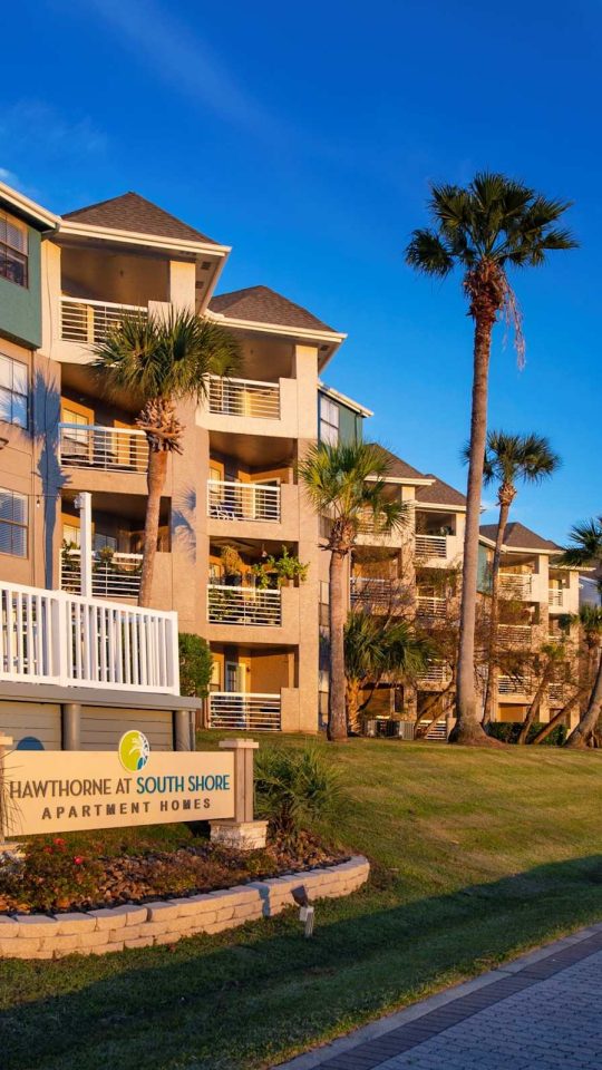 Waterfront apartment building exterior with monument sign, boardwalk and marina at Anchor at South Shore in League City, TX