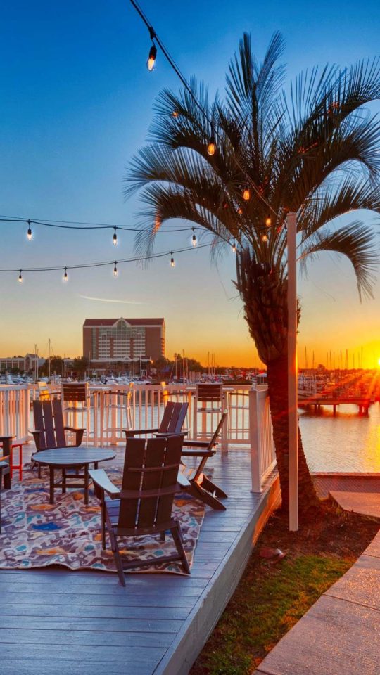 Waterfront marina deck with string lights and Adirondack chairs at sunset over South Shore Harbor at Anchor at South Shore in League City, TX