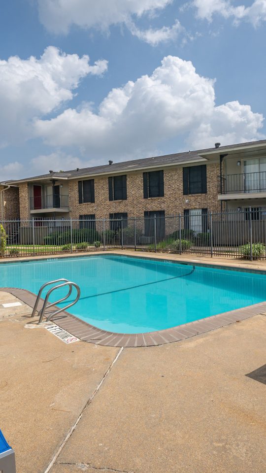 Sparkling swimming pool with sun deck and brick apartment buildings at Clear Creek Landing in Houston, TX