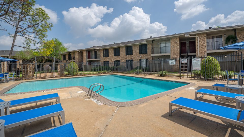 Sparkling swimming pool with sun deck and brick apartment buildings at Clear Creek Landing in Houston, TX
