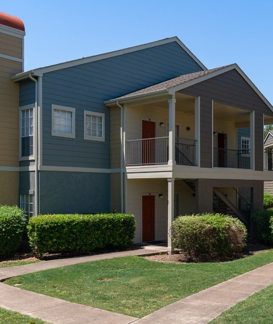 the exterior of an apartment complex with landscaping and trees at The Westmount at Three Fountains