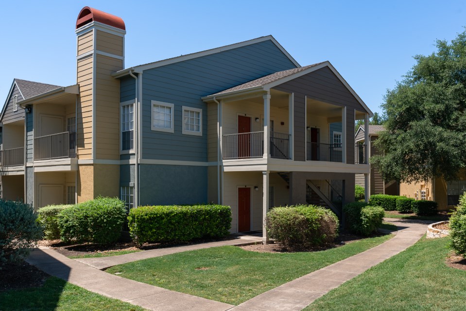the exterior of an apartment complex with landscaping and trees at The Westmount at Three Fountains