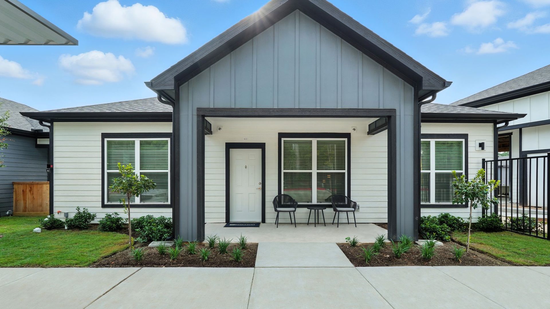 Two-Bedroom Homes for Rent in Conroe, TX - Soltera Rolling Pines - Modern Cottage Style Home Exterior With Covered Front Porch, Patio Chairs, Black Trim, And Fresh Landscaping Along Walkway.