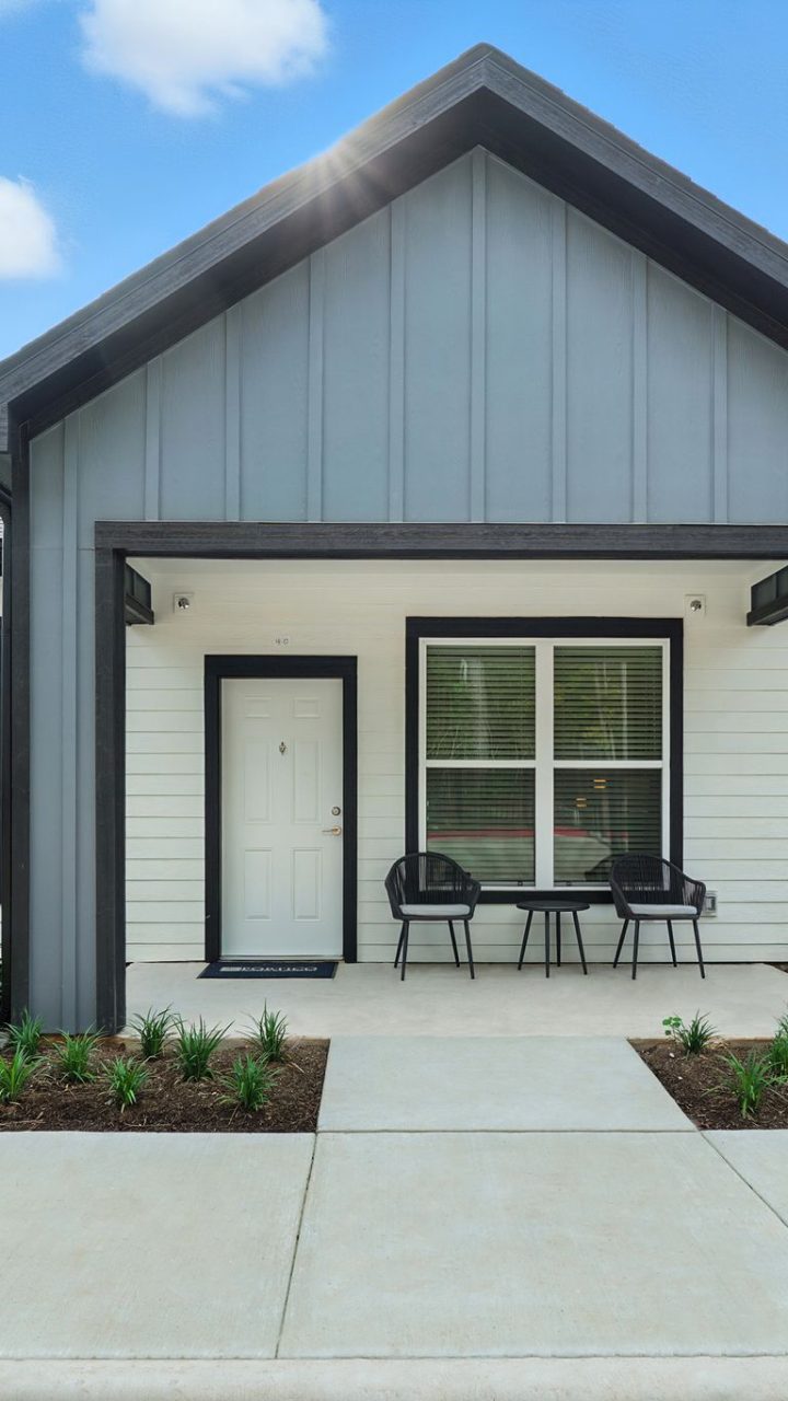 Two-Bedroom Homes for Rent in Conroe, TX - Soltera Rolling Pines - Modern Cottage Style Home Exterior With Covered Front Porch, Patio Chairs, Black Trim, And Fresh Landscaping Along Walkway.