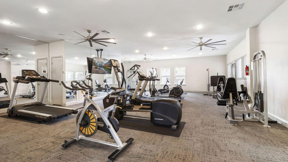 a gym room with treadmills, exercise equipment and ceiling fans at The  Adelene