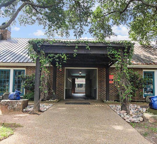 the entrance to a building with trees and bushes at The  Woodlands Apartments