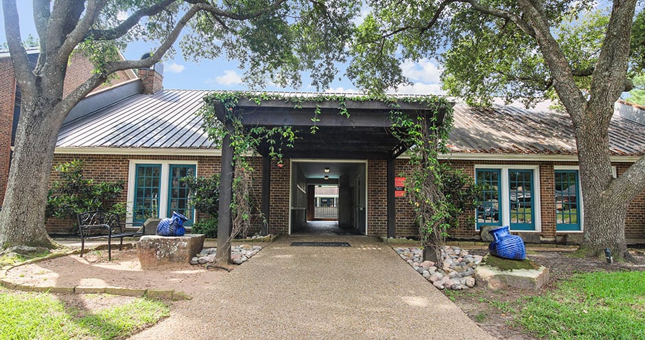 the entrance to a building with trees and bushes at The  Woodlands Apartments
