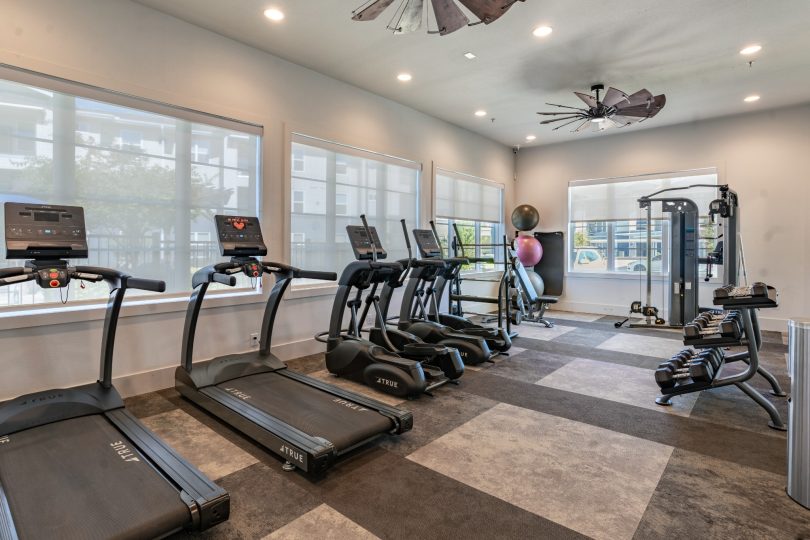 a gym room with tread machines and ceiling fans at The Landmark at Crowley