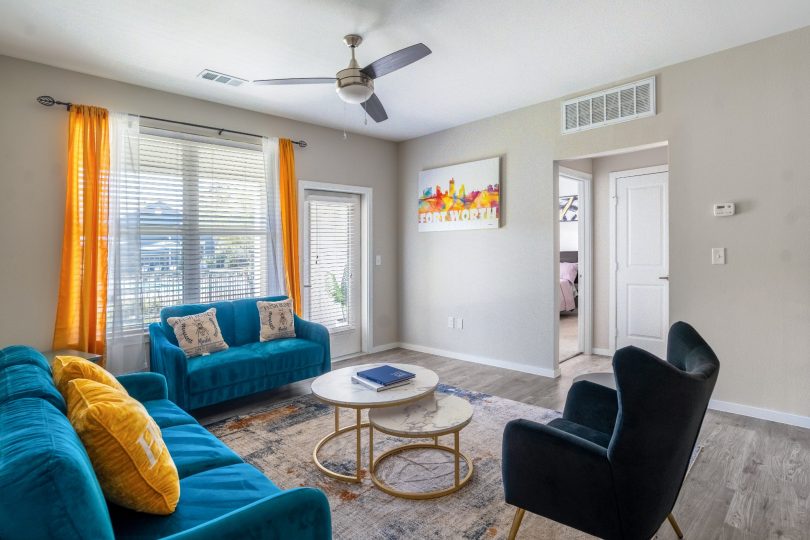 Furnished apartment living room with blue couches and a ceiling fan at The Landmark at Crowley