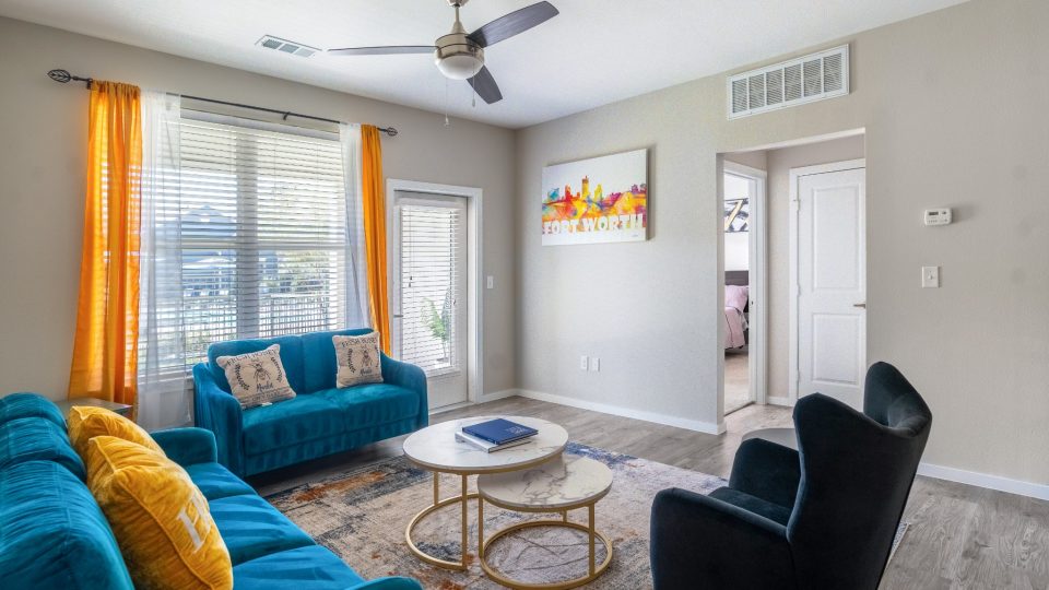 Furnished apartment living room with blue couches and a ceiling fan at The Landmark at Crowley