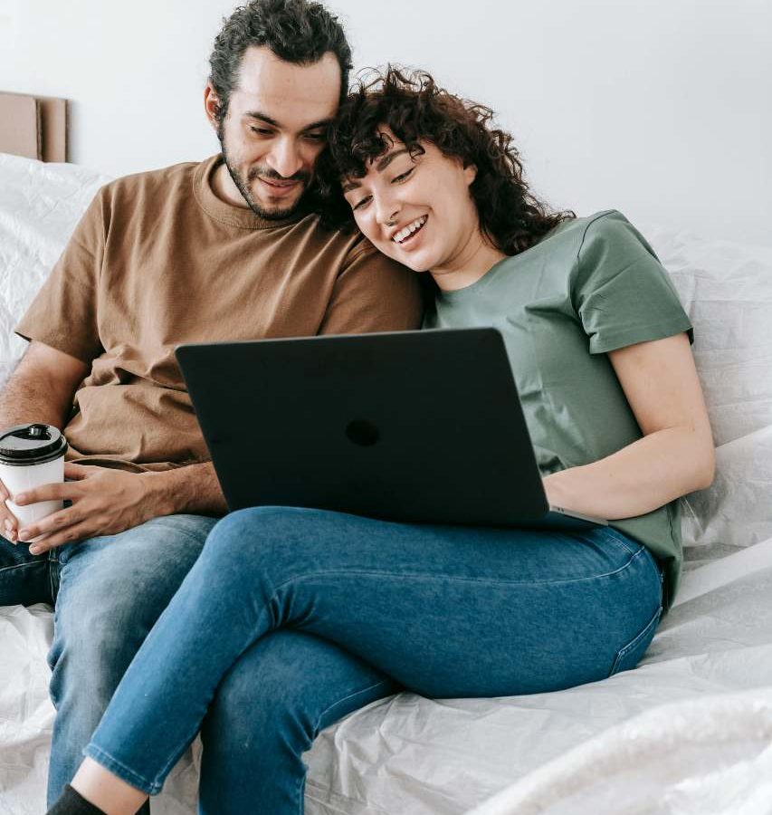 a man and woman sitting on a bed with a laptop at The Woodview