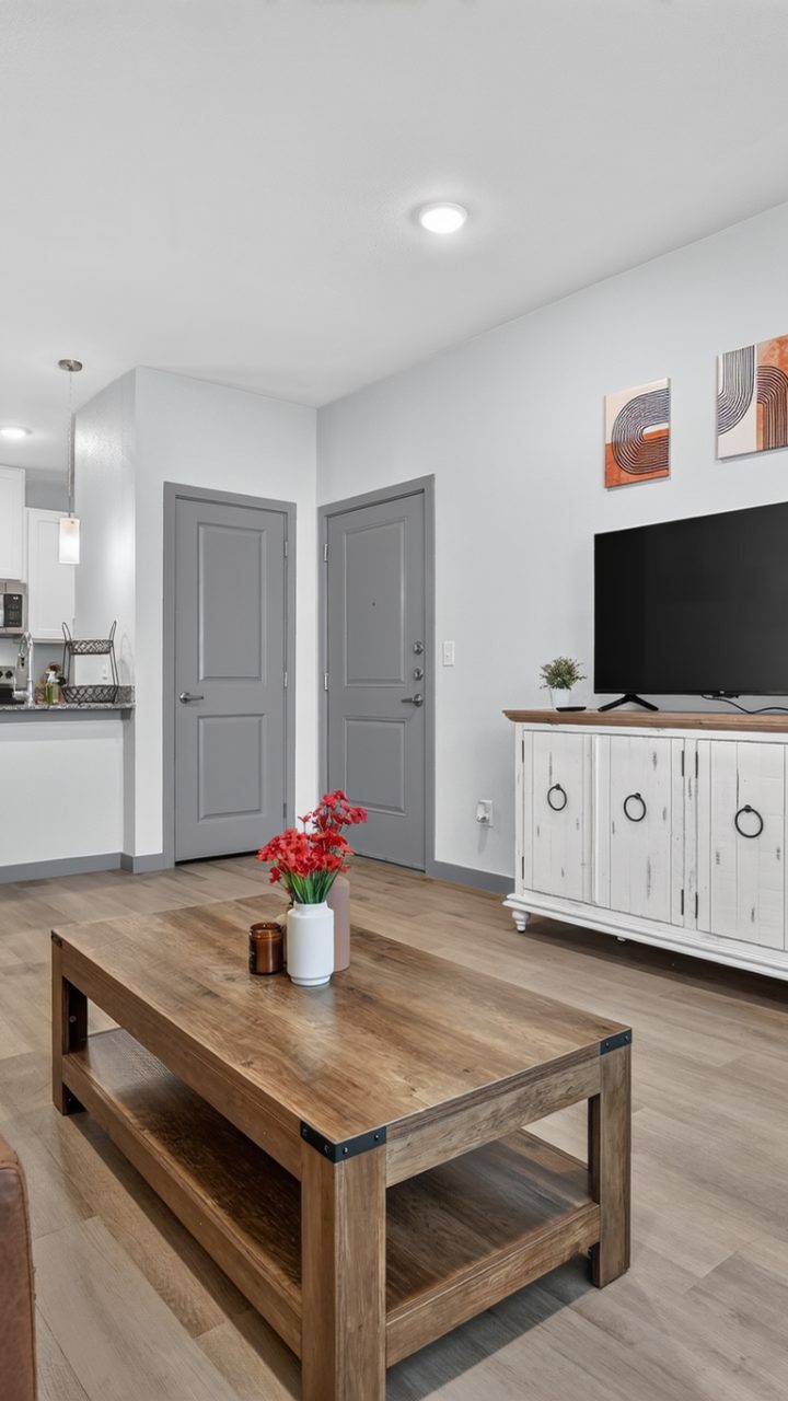 Union Chapel Rd living room with brown sofa, wood table, TV. Open kitchen has stainless appliances, white cabinets.