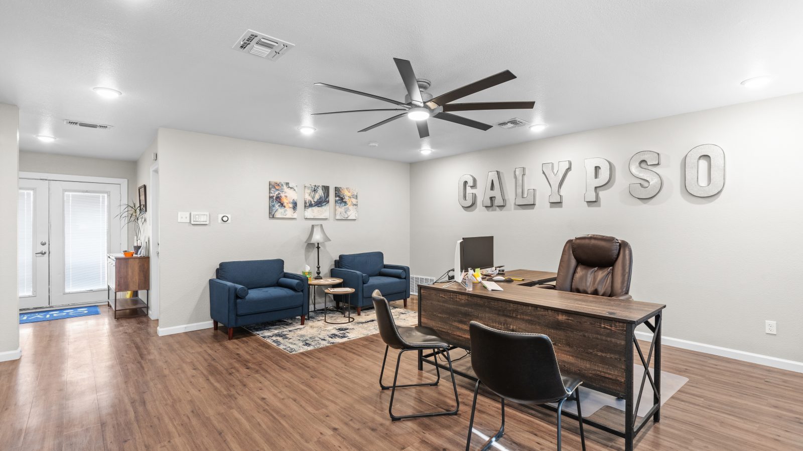 a living room with a ceiling fan and hardwood floors at The Calypso Apartments