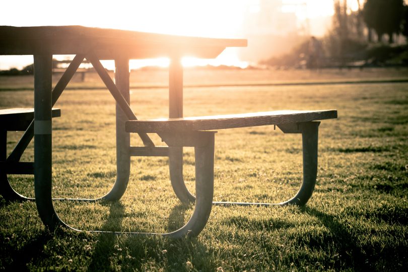 grey picnic table on grass field during sunset