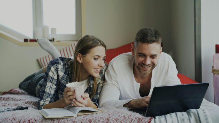 Couple lying on bed with laptop and coffee