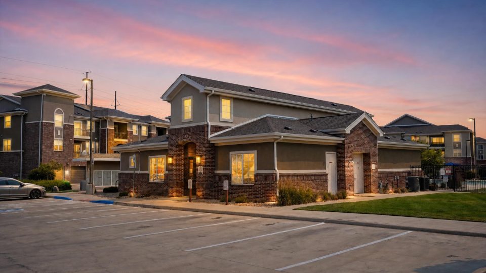 Outlook Blvd apartments. Modern brick clubhouse and buildings at sunset. Lit windows, empty parking lot.