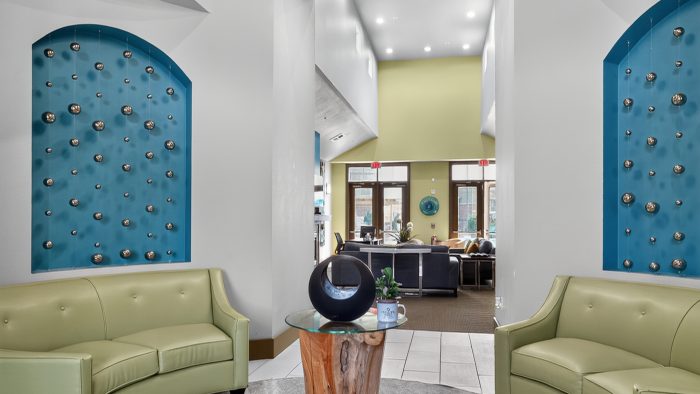 Modern foyer with two light green curved sofas, unique wood table, blue wall art, and lounge entrance.