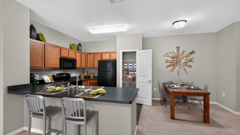 Open concept kitchen featuring wood cabinets, black appliances, and bar seating. Dining room with a wood table.