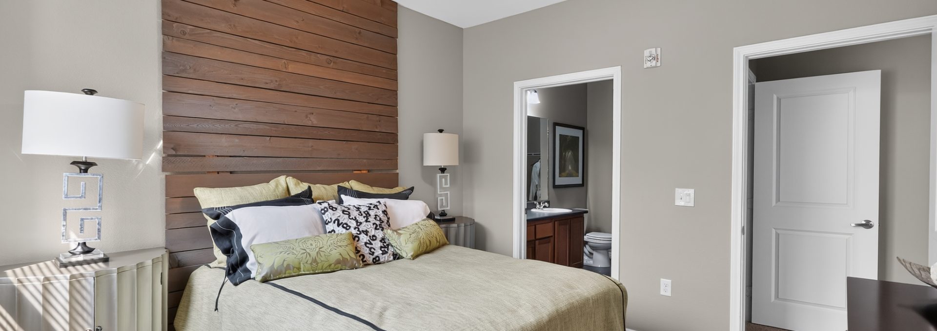 Bright Outlook Ridge Apartments bedroom with a queen bed, wood accent wall, ceiling fan, plush carpet, and private bath access.